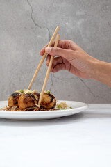 Hand with chopsticks holding a Takoyaki ball over a marble table