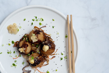 A plate of takoyaki with chopsticks over a marble table