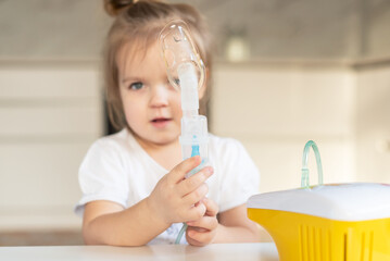 Little caucasian girl is breathing with special mask, which helps to stop asthma attack or relieve symptoms of respiratory disease. Child making inhalation with nebulizer at home