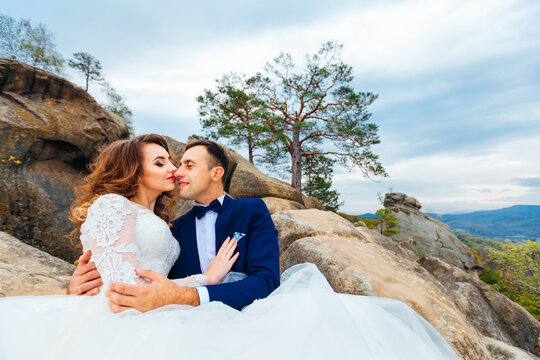 Close-up of newlyweds who sitting on the rocks embracing each other and wanting to kiss