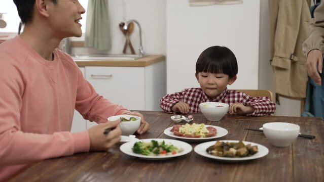 cute Asian boy saying wow as his mother putting a plate of delicious food on table at dinner. the woman applauds and praises her son as he is eating meat with spoon