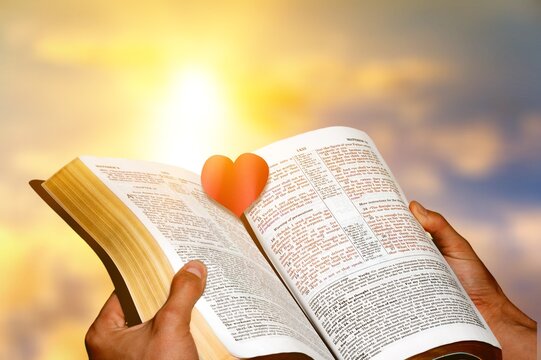 Open book and red heart in the center on sky background .