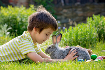 Cute child, playing with little bunny and easter eggs in a blooming garden, springtime