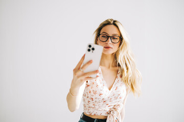 Fototapeta premium Young attractive caucasian woman in eyeglasses using mobile phone on white background.