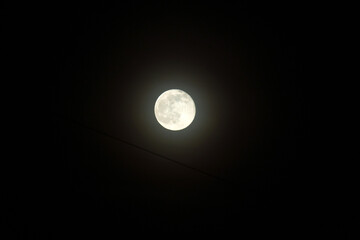 Close up shot of full moon set against dark black night sky. Electric wires, city at night
