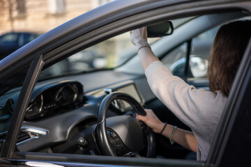 Woman adjusting the rearview mirror while sitting in the car on the driver's seat ripping behind the wheel