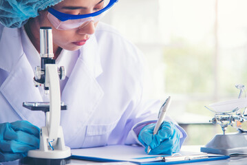 Woman scientist hand write note information in medical lab look at science microscope medical test,...