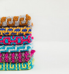 Stack of bright crochet clothes with geometric pattern on a white background. Colored knitted texture. Space for text. Needlework concept.