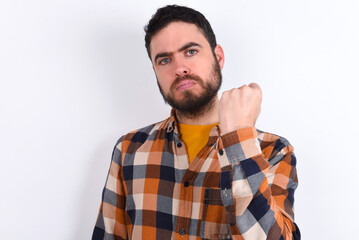 young caucasian man wearing plaid shirt over white background shows fist has annoyed face expression going to revenge or threaten someone makes serious look. I will show you who is boss