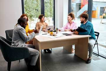 Fototapeta premium Group of diverse employee coworking together at workplace company. Portait of multi-ethnic creative team sitting behind desk in workspace, discussingm, having talk with documents and laptop