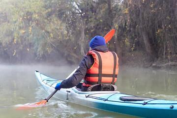 Man paddle kayak in the fog at the little river at autumn morning. Back view