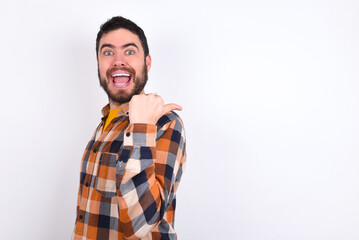 Fototapeta premium Impressed young caucasian man wearing plaid shirt over white background point back empty space