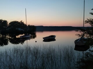 Pink sunset on a lake with its small boats reflected on the surface.
