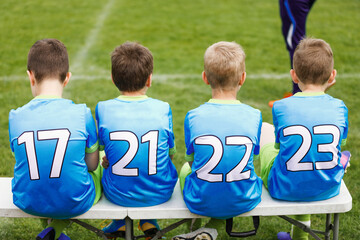 School football team. Soccer players sitting on sideline bench. Youth soccer players sitting together on substitute bench and watching match