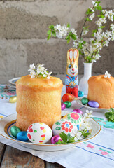 Happy Easter concept. Sweet bread with dried fruits and colored eggs. Holidays breakfast. Orthodox kulich. Festive table place setting decoration with paska, blossom twigs, bunny, chocolate egg.