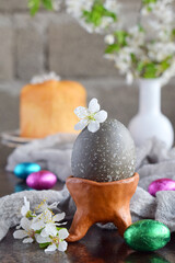 Obraz na płótnie Canvas Black colored egg and flowers on clay plate. Happy Easter card. Holidays breakfast concept. Festive table place setting decoration with blossom, bunny, chocolate eggs.
