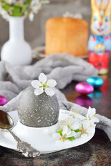 Obraz na płótnie Canvas Black colored egg and flowers on clay plate. Happy Easter card. Holidays breakfast concept. Festive table place setting decoration with blossom, bunny, chocolate eggs.