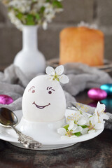 Obraz na płótnie Canvas Smiling white egg and flowers on clay plate. Happy Easter card. Holidays breakfast concept. Festive table place setting decoration with blossom, bunny, chocolate eggs.