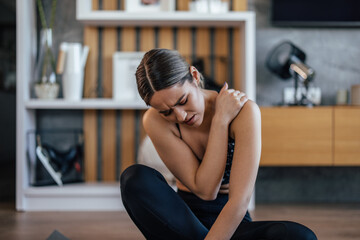 Girl having shoulder pain, sitting on a sports mat.