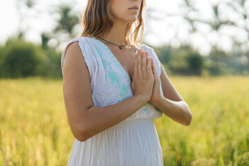 Fototapeta na wymiar Pregnant woman stand at the field with green grass and fold her hands in pray. Sunshine summer vibes