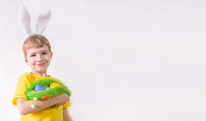 Happy child smiling in a yellow t-shirt in rabbit ears and with colorful eggs in a basket on a white background. Happy Easter concept with place for text.