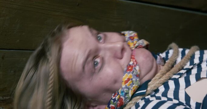 Scared tied woman with gag on mouth tries to break free from pirate captivity lying ON floor in wooden cabin of ship closeup