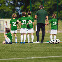 Square photo of young boys and soccer coach watching a football match. Youth reserve substitute players ready to play the tournament match. School soccer team in green jerseys with trainer