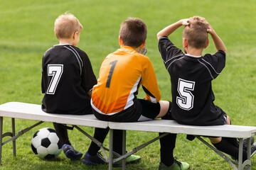 Soccer players sitting on sideline bench. School football team. Youth soccer players sitting together on substitute bench and watching match