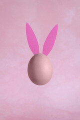 Single Egg with Bunny Ears on a Grunge Light Pink Background. Modern Minimalist Easter Holiday Composition with Chicken Egg ideal for Banner, Card, Greetings. No text. Funny  Levitating Egg.