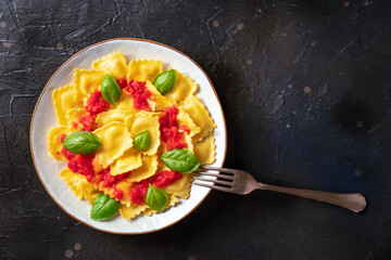 Ravioli with tomato sauce and basil on a plate, top shot with a fork. Italian dinner on a black slate background