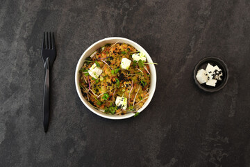 Healthy vegetarian bowl with red lentil, feta cheese and greens with plastic fork isolated on dark background. Food delivery service and daily ration concept.