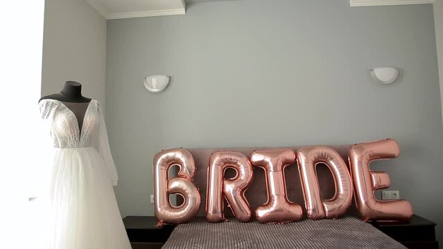 Foil helium balls of pink color. Pink gel balls with the word bride on the bed and the bride's dress on the mannequin. Letters