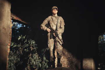 a soldier of ukraine with a backpack on his back in a gray camouflage uniform, in tactical glasses and in a cap with a machine gun in his hands stands in the sun and looks into the distance