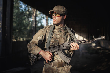 serious stern male soldier in a gray camouflage uniform, wearing tactical glasses and a cap with a black machine gun in his hands inside a large authorized building