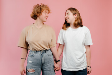 LGBT Lesbian couple happiness concept. Portrait of teenage lesbian girls holding hands on pink background, looking at each other