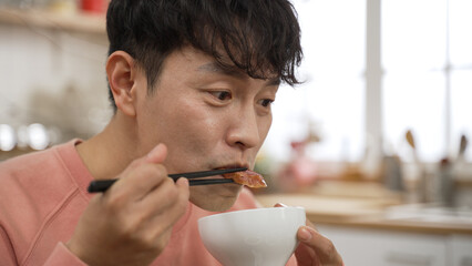 closeup with headshot cheerful asian man enjoying tasty meat with chopsticks in the dining room at...