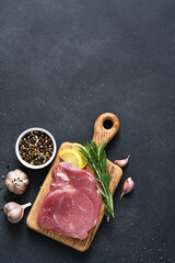 Fresh raw meat on a wooden board with rosemary and lemon on a black background, pork