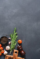 Spices on black concrete background. Wooden board, rosemary and tomatoes on the kitchen table, top view.