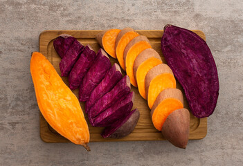 Whole and cut raw orange and purple sweet potato on cutting board closeup, top view