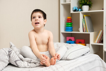 Portrait of a 4-year-old naked boy looking sideways in a children's room against a backdrop of toys