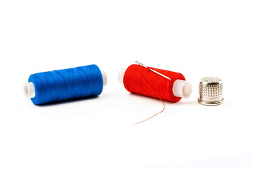 A spool of blue and red threads with a needle and a thimble on a white isolated background.