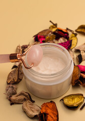 Female face body care concept. Morning beauty routine. Massage roller, container with cream, part of flowers. Selective focus, close-up