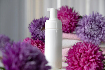 White bottle of beauty product mock up with flowers around, pink purple asters. Face care, anti-aging, exfoliating cosmetic. Essential oil, aromatherapy.
