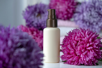 Bottle of beauty product mock up with flowers around, pink purple asters. Face care, anti-aging, exfoliating cosmetic. Organic SPA cosmetics with herbal ingredients.