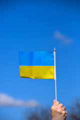 Arm holds waving flag of Ukraine on blue sky background,national blue and yellow flag photo, patriot of Ukraine sign