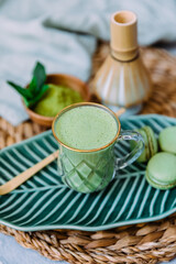 Matcha green latte and macaroons dessert with matcha powder, bamboo whisk and spoon on a blue background. Japanese tea ceremony. Top view, flat lay.