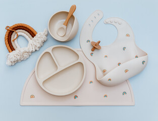 Flat lay composition with silicone baby bib and beige dishware on blue background. Flat lay, top view
