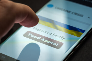 Close-up finger pressing fund appeal button on smartphone screen. Donation money online concept