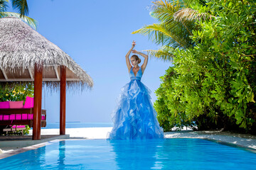 Elegant fashion model near the pool. Glamour woman in elegant long gown dress on the Maldives...