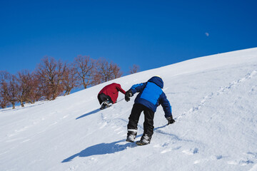 People climb the mountain on an icy slope. Climbing to the top of the mountain. Winter hike. A child on a journey through the mountains, snow under his feet.